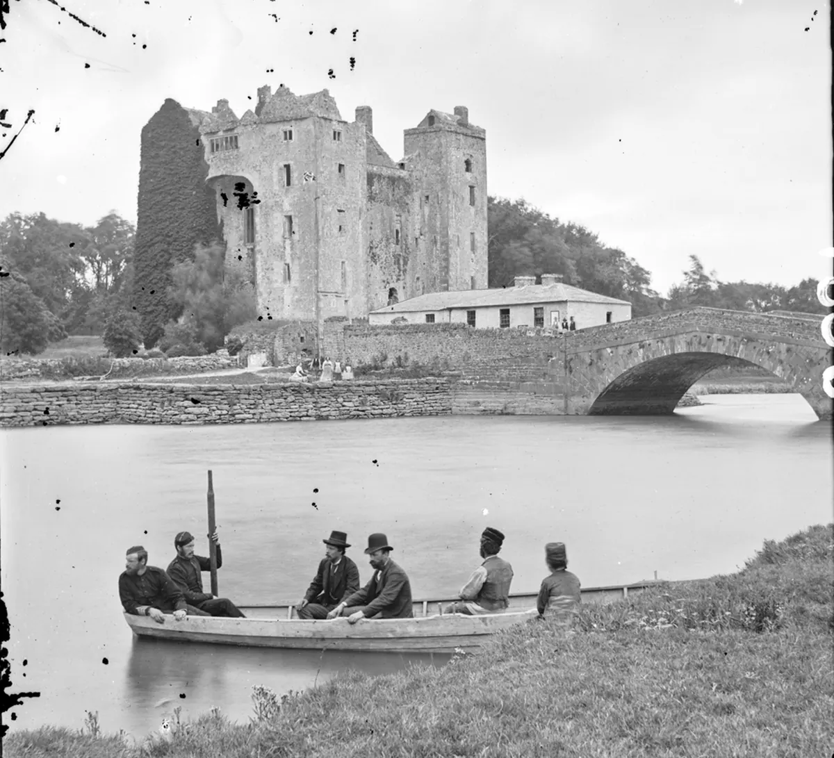 石橋の背後に建つBunratty Castleの白黒写真。手前にはボートとダークコートを着た男たちが写っている