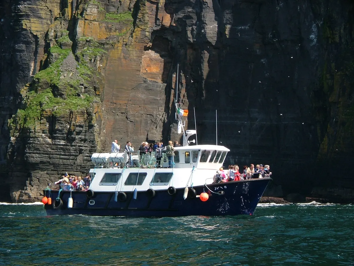 Ein weiß-blaues Passagierschiff mit Menschen an Deck am Fuße hoher, dunkler Steilküsten