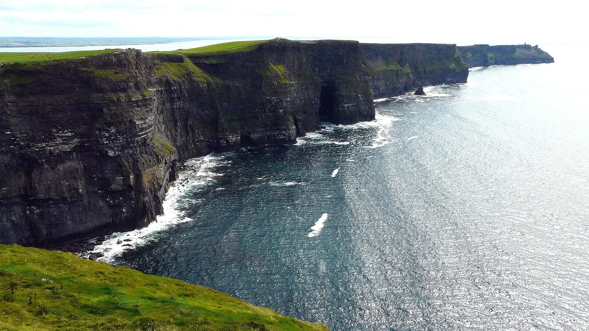 Die Cliffs of Moher, hohe, dunkle Steilküsten, die sich unter einem strahlenden Himmel entlang der Atlantikküste erstrecken