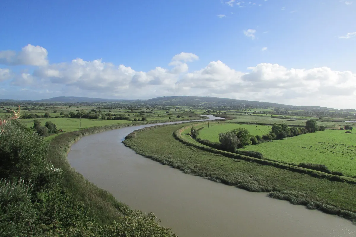 Il fiume Ratty che serpeggia tra campi verdi sotto il Bunratty Castle, con l'estuario dello Shannon e le colline in lontananza